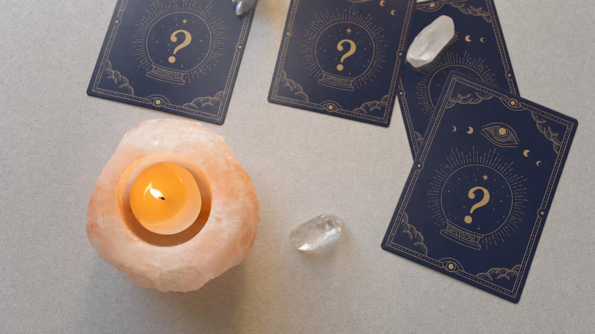 Quatre cartes de l'oracle face cachée, une bougie dans un photophore en sel rose et des cristaux de quartz sur une surface claire